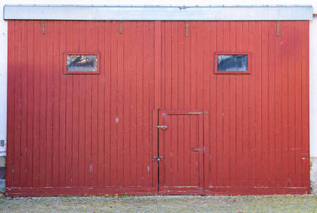 Very tall old red barn door with two small windows and a doorの写真素材