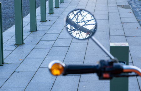 Looking into the mirror of a motorcycle in which the bare branches of a tree can be seenの写真素材