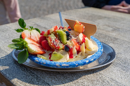 Bowl with delicious ice cream and lots of fruits on a wooden table of an ice cream shopの写真素材