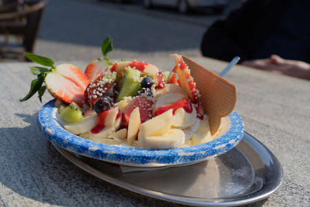 Bowl with delicious ice cream and lots of fruits on a wooden table of an ice cream shopの写真素材