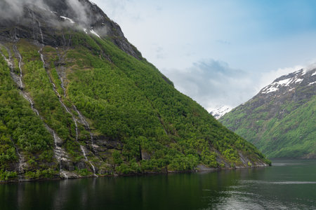 Beautiful landscape with snowy mountain peaks and waterfalls in Geiranger fjord, Norwayの写真素材