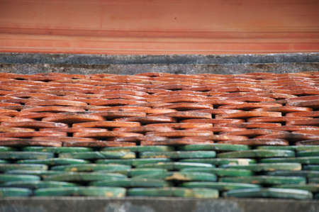 Shallow perspective view of green and red terracotta roof tiles on a buddhist temple in Asia.の写真素材