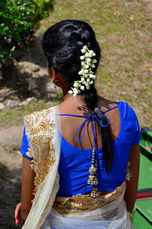 Rear view of a beautiful plait of black hair adorned with white jasmine flowers as worn by a young Indian girl in a blue and gold sari.の写真素材