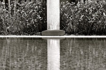 Azure blue swimming pool with symmetrical reflected image of a white concrete pillar.