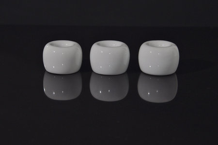 A row of white ceramic cylinders on a shiny black reflective surface, showing an inverted mirror...