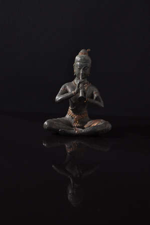 Bronze buddha statue on a black reflective surface with an inverted mirror image.の写真素材