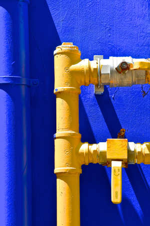 Heavy duty industrial yellow, metal water pipes and taps, isolated against a dark blue background.の写真素材