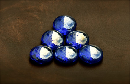 Small triangle of iridescent blue glass beads isolated on a dark wood background.