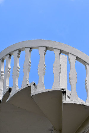 Upward perspective view of an exterior white stone spiral staircase against a clear blue sky...