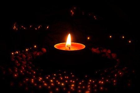 Side view of a burning tealight candle isolated against a warm background of partially illuminated...