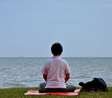 Lone Asian lady practicing yoga and meditating by the sea.の写真素材
