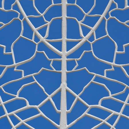A close up view of a white cast iron filigree trellis pattern isolated against a blue sky background.の写真素材