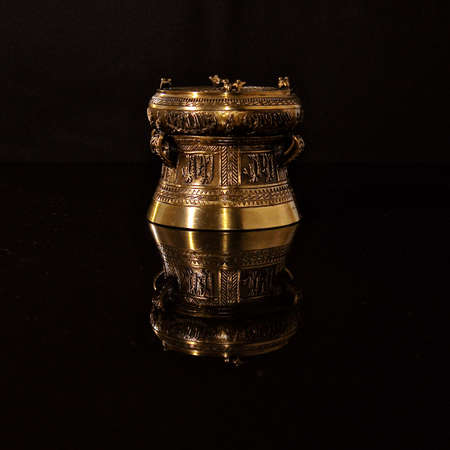 Ornate bronze ornament on a shiny black reflective surface, showing an inverted mirror image.の写真素材