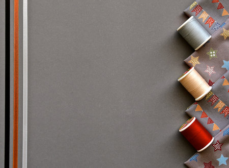 A birds eye view of sewing accessories with cotton, silk ribbons and material on a grey background.