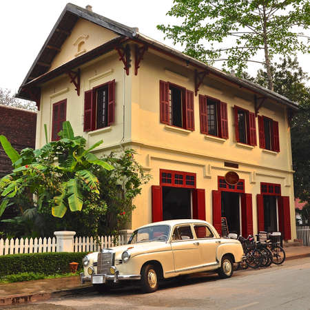 Luxury cream vintage car parked outside a colonial building with red wooden shutters.のeditorial素材