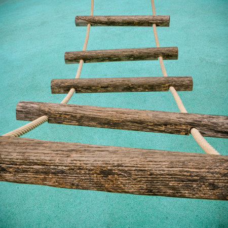 A perspective view of a rope ladder with wooden rungs on a children's climbing frame.
