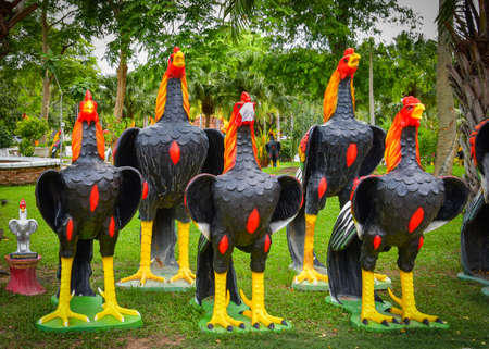 Rows of socially distanced large rooster statues in a buddhist temple complex in Thailand. One of the roosters is wearing a surgical facemask as required during lockdown in the covid pandemic.の写真素材