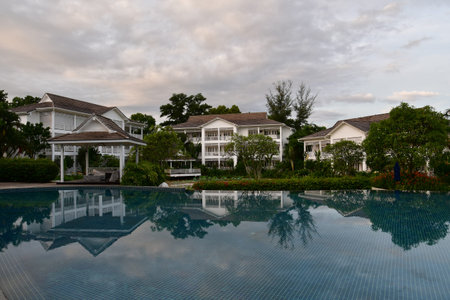 A white colonial building in a tropical garden setting with a perfect mirror image reflection in the...