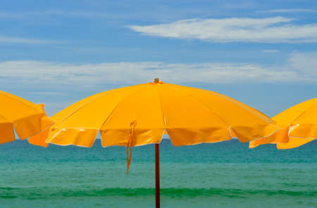A tropical beach scene with yellow parasols against a backgound of clear blue skies and blue green seas.の写真素材