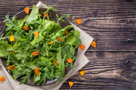 Arugula salad with marigold petals on wooden background, top view, diet foodの写真素材