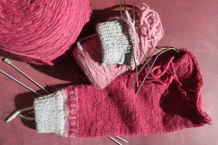 Knitting needles, yarn and woolen sleeve on a red background