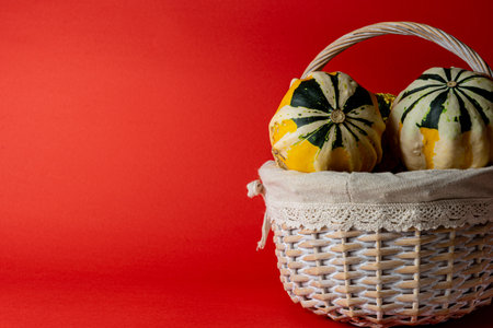 Colorful decorative pumpkins in a wicker basket on a red backgroundの写真素材