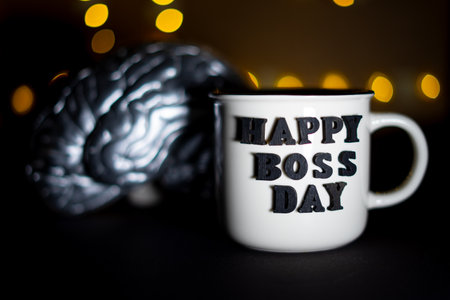 Mug of coffee and siver brain with the inscription Happy Boss's Day on a black background. Selective focus.の写真素材