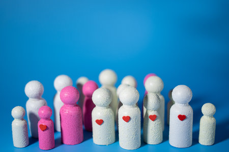 A group of white and pink figurines with small red hearts on their chests, symbolizing unity, love, and community support, against a blue background.の写真素材