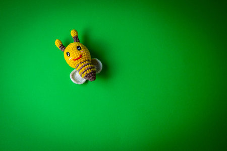 Handmade knitted toy bee on a green background. Copy space.