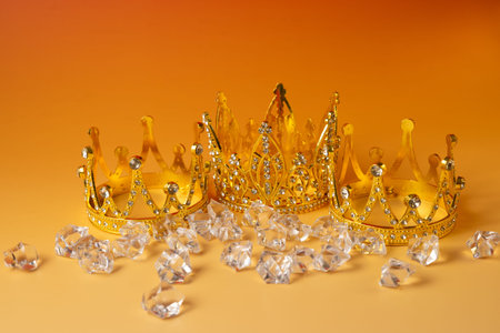 Golden crowns with diamonds on orange background, close-up