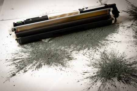 Printer toner cartridge placed on sheets of white paper and scattered with toner powderの写真素材