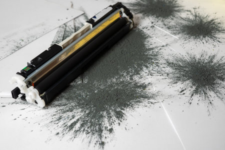 Printer toner cartridge placed on sheets of white paper and scattered with toner powderの写真素材