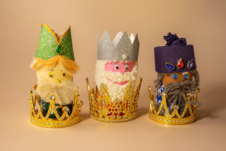 Three handmade Three Kings figurines placed inside of crowns are displayed on a beige background, symbolizing Epiphany celebration on January 6. Selective focus.の写真素材