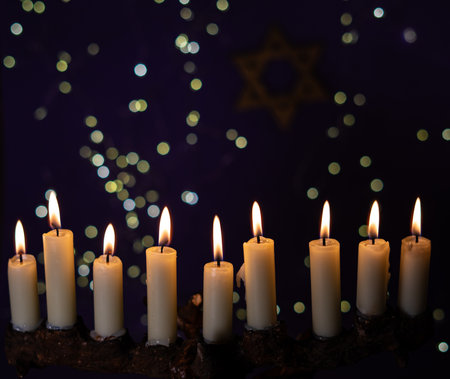 A menorah with nine glowing candles is placed in front of a Star of David on a purple background, representing Hanukkah.の写真素材