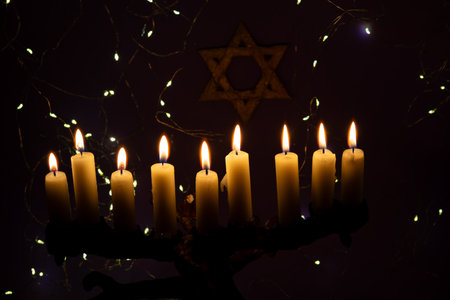 A menorah with nine glowing candles is placed in front of a Star of David on a purple background, representing Hanukkah.の写真素材