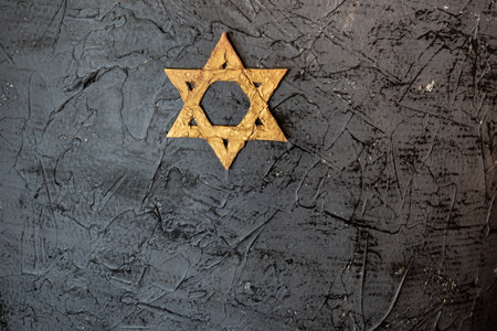 A golden Star of David placed on a textured black surface represents Jewish heritage and Holocaust remembranceの写真素材