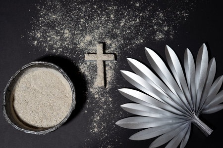 A bowl filled with ashes beside a cross shape and silver palm leaf on a dark background illustrates...