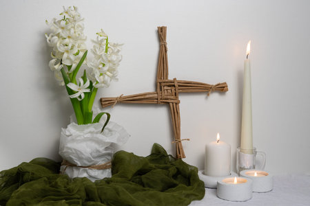 A Saint Brigidâs Imbolc altar with a woven Brigidâs cross, white hyacinth, lit candles, and green cloth is arranged against a light background to symbolizeearly spring.の写真素材