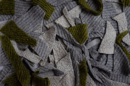 Grey and olive green wool fabric scraps scattered across the surface illustrate textile waste, craft...