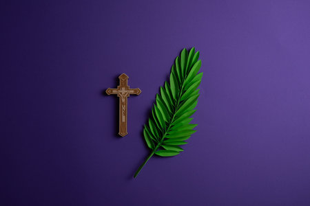 Wooden cross and palm leaf on a purple background, top view