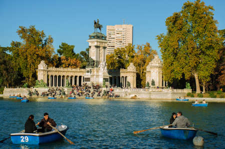 Personas remando en lago del parque El Retiro mientras otros toman sol durante el otoño (Madrid-España)のeditorial素材