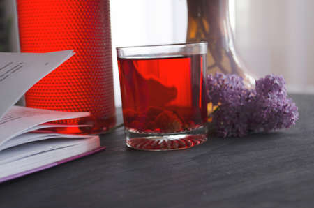 Still life with a bouquet of lilacs and compote of berries. A glass of compote, a jug, a bouquet, a book and glasses on a dark wooden table. Still life near the window.の写真素材