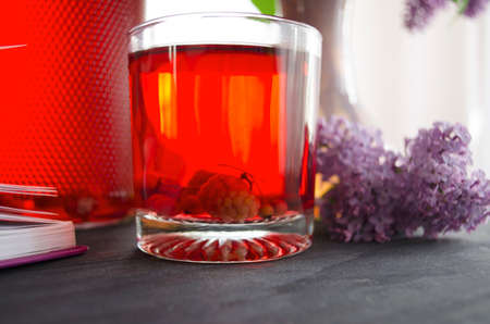 Still life with a bouquet of lilacs and compote of berries. A glass of compote, a jug, a bouquet, a book and glasses on a dark wooden table. Still life near the window.の写真素材