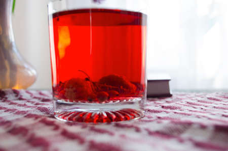Still life with a bouquet of lilacs and compote of berries. A glass of compote, a jug, a bouquet, a book and glasses on a dark wooden table. Still life near the window.の写真素材