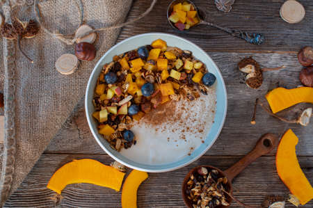 Breakfast bowl with sauteed apples and pumpkin, homemade granola and blueberries. Served on wooden table background. overhead viewの写真素材