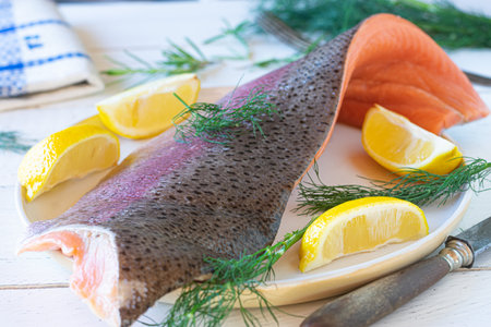 Half Salmon trout with skin on a white wooden table with lemon and dill. Raw, uncooked and freshの写真素材