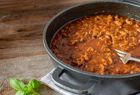 Stew pot with italian duck ragout cooked with root vegetable, tomatoes and herbs. Served isolated on wooden table. Side view with copy spaceの写真素材