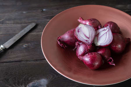Red onions in a bowl. Heap of Spanish onions in a bowl with cross section on rustic and wooden table. Side view with copy spaceの写真素材