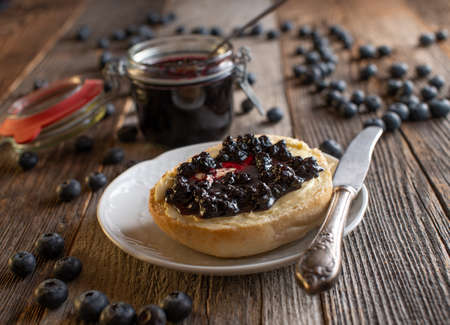 Breakfast Bun with homemade blueberry jam served on a plate with knife and jar on wooden table background.の写真素材