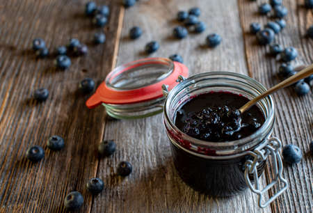 Homemade blueberry jam in a jar with spoon isolated on wooden table backgroundの写真素材